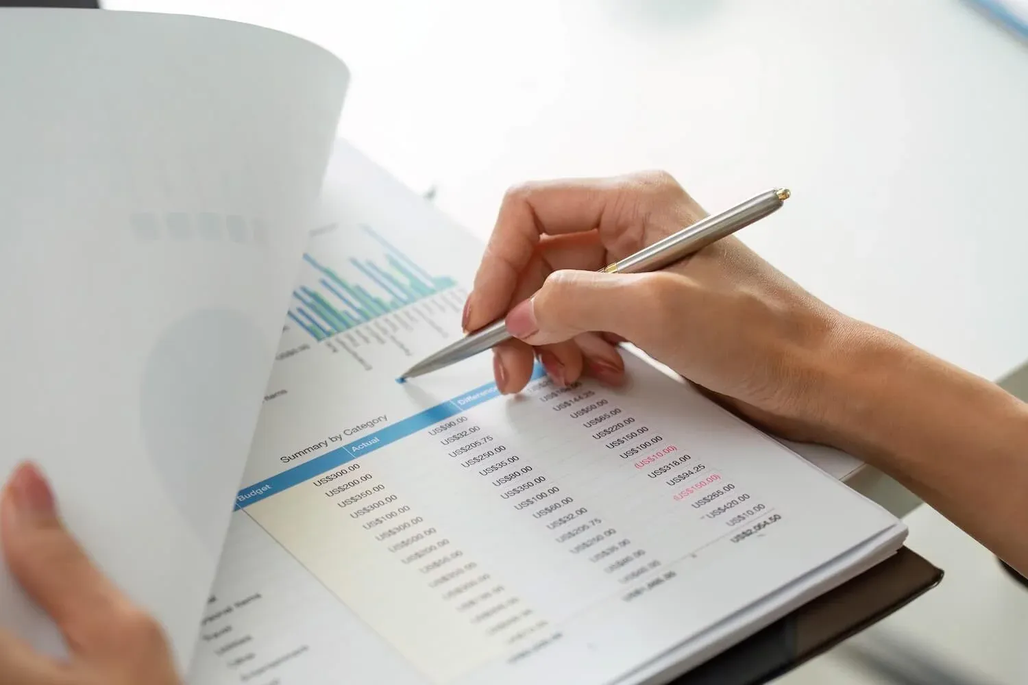 Hand mit Stift zeigt auf eine Übersicht mit Kennzahlen und Diagrammen – symbolisch für die Erstellung und Analyse von Jahresabschlüssen.